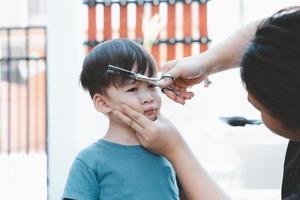 une mère asiatique coupe les cheveux de son fils toute seule à la maison. bonnes idées de coupe de cheveux pour les enfants. les mères sont heureuses de couper les cheveux de leurs enfants. photo