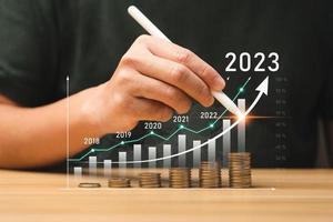 homme d'affaires planifiant la croissance de l'entreprise 2023 sur le bureau avec graphique graphique hologramme virtuel. calculer le revenu et le profit sur les investissements et une augmentation des indicateurs de croissance positive, le rendement des actions photo