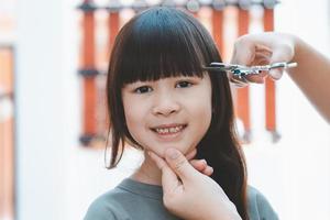 les mains des femmes pour couper les cheveux avant ou la frange pour une jolie fille asiatique à la maison. les mères sont heureuses de couper les cheveux de leurs enfants. concept de soins capillaires photo