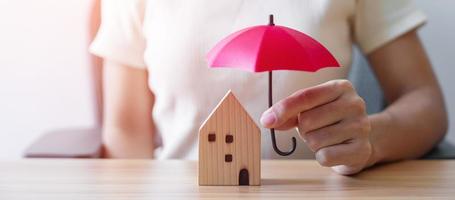 main de femme d'affaires tenant le modèle de maison en bois de couverture de parapluie rouge. concepts d'immobilier, d'assurance et de propriété photo