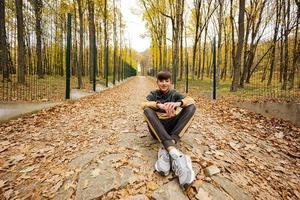 garçon adolescent s'asseoir sur le chemin à la forêt d'automne d'automne. photo