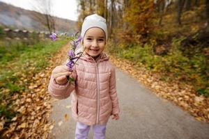 petite fille tient dans la main la campanule, cloches de fleurs violettes dans la forêt d'automne. photo