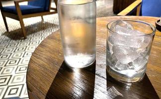 mise au point sélective, un verre transparent rempli de glace et une bouteille en verre transparent contient de l'eau minérale froide se trouve sur une table en bois photo