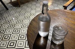 mise au point sélective, un verre transparent rempli de glace et une bouteille en verre transparent contient de l'eau minérale froide se trouve sur une table en bois photo