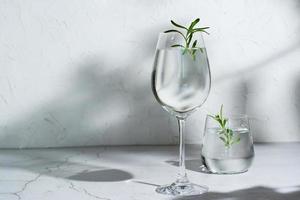 deux verres d'eau rafraîchissante et de romarin sur la table à l'ombre des feuilles d'arbres photo