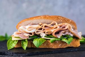 sandwich prêt à manger avec bacon, concombre, fromage et basilic sur la table. restauration rapide à domicile. fermer photo