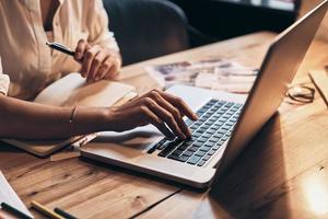 toujours en ligne. gros plan d'une jeune femme travaillant à l'aide d'un ordinateur tout en étant assise dans son atelier photo