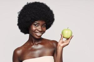 portrait de la belle jeune femme africaine tenant une pomme verte et souriant debout sur fond gris photo