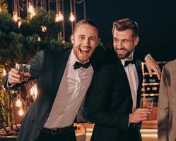 deux beaux hommes en costume buvant du whisky et souriant tout en passant du temps à la fête photo