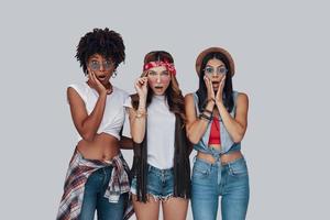 trois jeunes femmes surprises faisant une grimace et regardant la caméra en se tenant debout sur fond gris photo