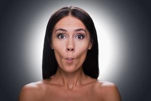 beauté ludique. portrait d'une belle jeune femme torse nu regardant la caméra et grimaçant en se tenant debout sur fond gris photo