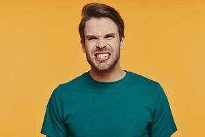 portrait d'un jeune homme en colère regardant la caméra et faisant une grimace en se tenant debout sur fond jaune photo