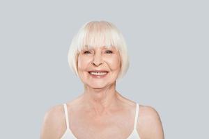 profiter de la vie. belle femme âgée regardant la caméra et souriant en se tenant debout sur fond gris photo