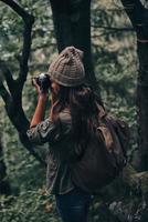 joli coup. jeune femme moderne avec sac à dos photographier la nature lors d'une randonnée dans les bois photo