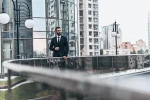 perdu dans les pensées. beau jeune homme en costume complet regardant loin tout en se tenant à l'extérieur photo