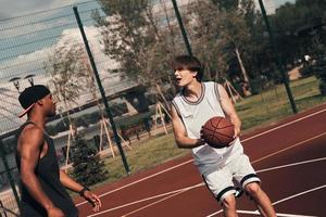 jouer dur. deux jeunes hommes en vêtements de sport jouant au basket tout en passant du temps à l'extérieur photo