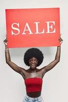 heureuse jeune femme africaine tenant une bannière de vente et souriant debout sur fond gris photo