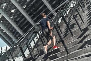 prêt à surmonter n'importe quel obstacle. toute la longueur du jeune homme en vêtements de sport qui monte les escaliers tout en faisant de l'exercice à l'extérieur photo