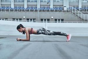 son corps est parfait. belle jeune femme en vêtements de sport gardant la position de la planche tout en faisant de l'exercice à l'extérieur photo