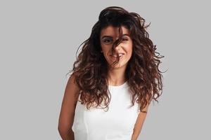 super coiffure. séduisante jeune femme regardant la caméra et souriant en se tenant debout sur fond gris photo