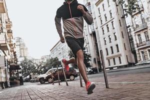 sur le chemin de la grande forme. gros plan sur un jeune homme en vêtements de sport courant le long de la rue de la ville photo