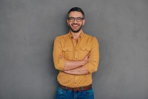 confiant et réussi. homme mûr confiant tenant la main sur le menton et regardant la caméra avec le sourire en se tenant debout sur fond gris photo