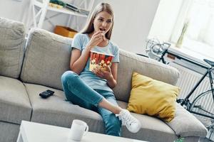 belle jeune femme mangeant du pop-corn en regardant la télévision sur le canapé à la maison photo