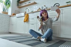 jeune femme portant un petit chien et faisant du selfie assis par terre à la cuisine photo