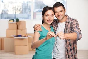 clé de leur nouvelle maison. heureux jeune couple debout près de l'autre et souriant tout en tenant la clé de la maison photo