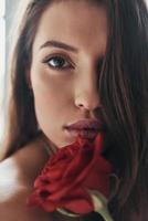 suprêmement sensuel. jolie jeune femme tenant une rose rouge et regardant la caméra tout en passant du temps à la maison photo
