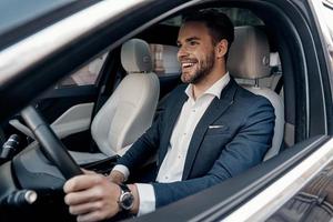 homme de style et de statut. beau jeune homme en costume complet souriant en conduisant une voiture photo