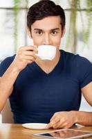 prendre un café au restaurant. beau jeune homme buvant du café au restaurant et souriant tandis que tablette numérique posée sur la table photo