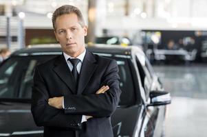 confiant dans son choix. homme mature aux cheveux gris en tenues de soirée debout devant la voiture et regardant la caméra photo