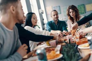 choisir la meilleure tranche. groupe de jeunes en tenue décontractée cueillant une pizza et souriant tout en dînant à l'intérieur photo