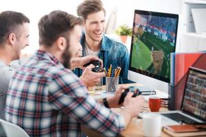 tester un nouveau jeu. Trois jeunes hommes jouant à des jeux informatiques tout en étant assis au bureau dans le bureau photo