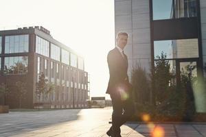 homme mûr confiant en costume complet marchant près des immeubles de bureaux à l'extérieur photo