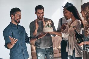 le temps de faire un vœu. heureux jeune homme gesticulant et souriant tout en célébrant son anniversaire entre amis photo