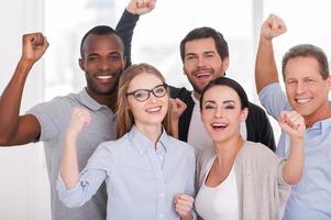 équipe commerciale heureuse. groupe d'hommes d'affaires joyeux en tenue décontractée debout près l'un de l'autre et gardant les bras levés photo