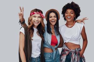 trois jolies jeunes femmes élégantes regardant la caméra et souriant en se tenant debout sur fond gris photo