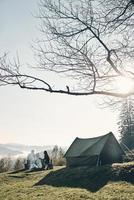 air frais et vue parfaite. jeune couple prenant un café le matin assis près de la tente dans les montagnes photo