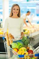 je fais toujours un choix sain. belle jeune femme tenant la main sur le panier et souriant tout en se tenant dans un magasin d'alimentation photo