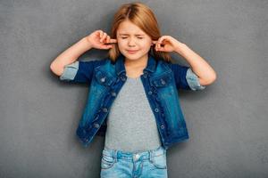 je n'écoute pas belle petite fille couvrant les oreilles avec les mains et gardant les yeux fermés en se tenant debout sur fond gris photo