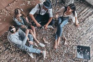 sortir avec des copains. vue de dessus de jeunes gens modernes versant du champagne assis sur le sol avec des confettis autour photo