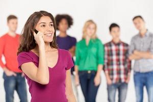 toujours en contact. joyeuse jeune femme parlant au téléphone mobile pendant que ses amis se tiennent sur le fond photo