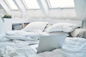 image d'un ordinateur portable posé sur un lit avec des oreillers et un nanket autour photo