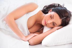 beaux rêves. belle jeune femme allongée dans son lit et gardant les yeux fermés tout en étant recouverte d'une couverture photo