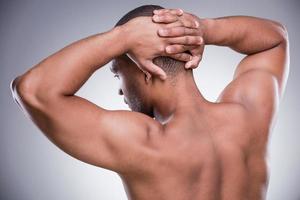 fort et athlétique. vue arrière du jeune homme africain tenant les mains derrière la tête en se tenant debout isolé sur fond gris photo