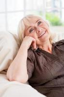 perdu dans les pensées. femme âgée réfléchie tenant la main sur le menton et souriant tout en étant assis sur une chaise photo