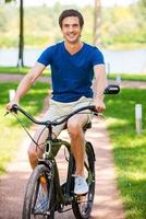 vélo dans le parc. heureux jeune homme à vélo dans le parc et souriant à vous photo