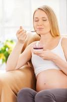 rêverie de jour de femme enceinte. femme enceinte heureuse assise sur la chaise et mangeant du yaourt photo